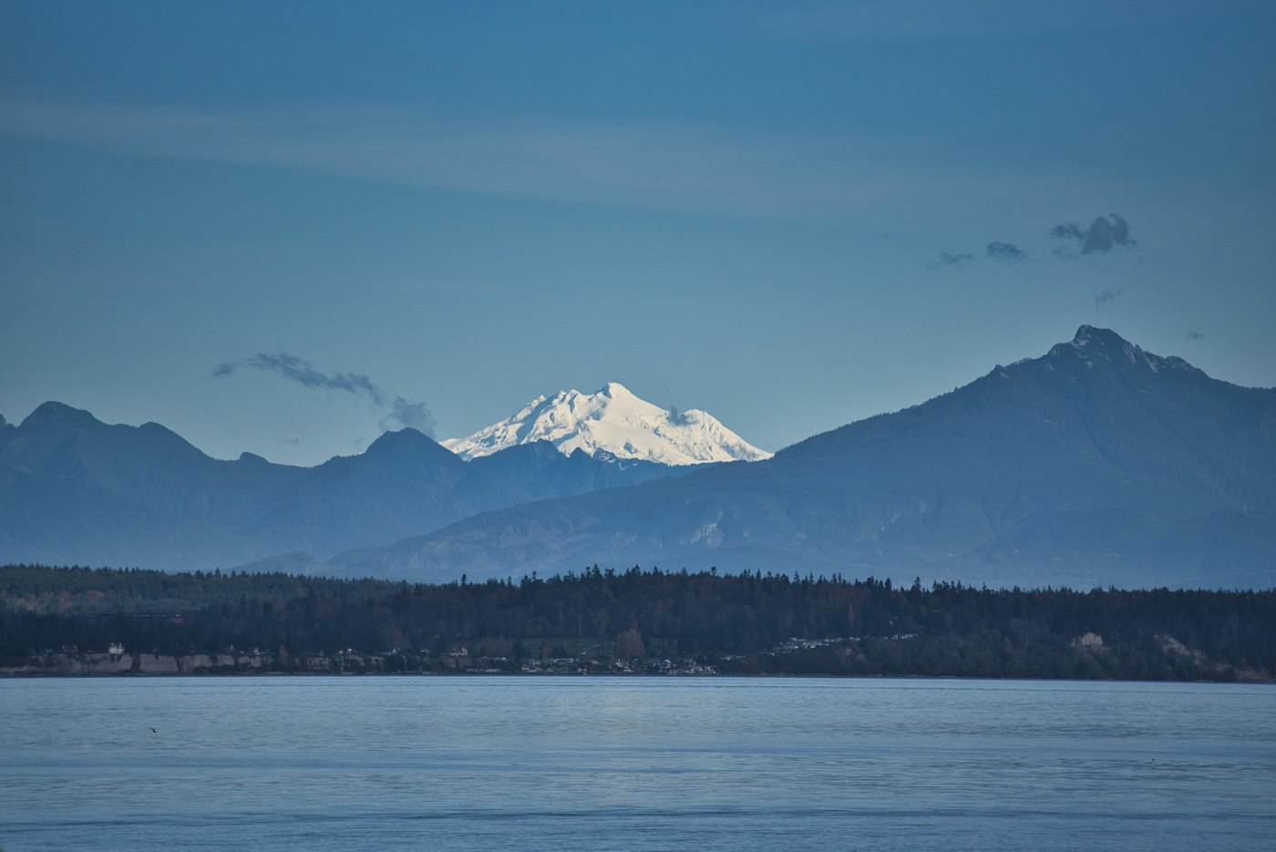 Snow-capped Mount Baker rising behind dark hills across the water